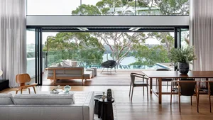 Modern living room with a water view, featuring a gray sofa, wooden furniture, and a glass wall.