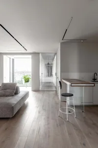 A modern living space featuring wooden flooring, glass partitions, and metallic elements.
