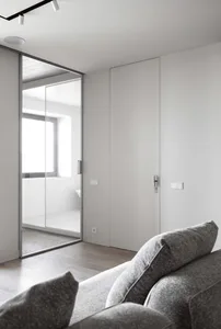 Modern minimalist living room with gray sofa, white walls, and glass sliding doors.