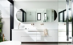 Modern white bathroom interior with sleek white vanity, large oval mirror, and textured wall tiles.