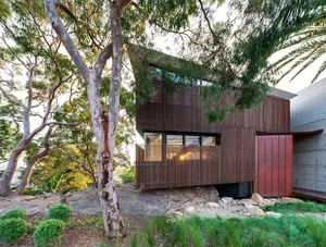 A modern house with a wooden exterior and large windows surrounded by greenery.