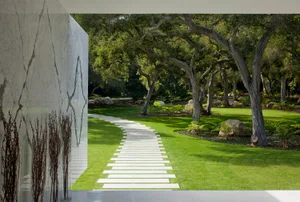 A white-tiled pathway leading through a green, grassy area surrounded by trees.