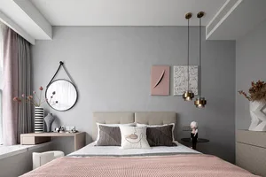 A minimalist bedroom with a grey accent wall, featuring a bed with geometrically patterned pillows, a round mirror, and abstr