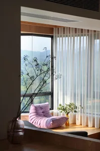 Minimalist living room with a purple upholstered chair, transparent curtains, and a view of green mountains.