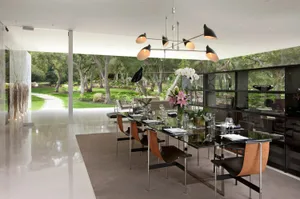 Modern dining room featuring a sleek, minimalist design with a glass chandelier and stylish furniture.