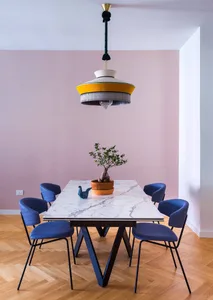 A modern dining room with a marble table, blue chairs, and a yellow lamp hanging from the ceiling.