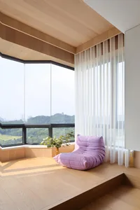 Modern window seat with a purple cushion and green plants, framed by large windows and wooden flooring.