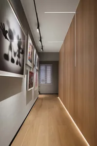 Long corridor with modern lighting fixtures, framed art, and wooden flooring.