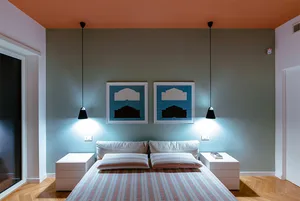 A photograph of a modern minimalist bedroom with a double bed featuring a striped blue, white, and red bedspread, minimalisti