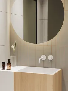 A minimalist bathroom featuring ceramic tiles, a wooden vanity, and a round mirror.