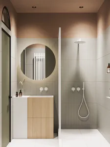 A modern bathroom with white tiles and light wood accents, featuring a circular mirror, wall-mounted sink, and a walk-in show