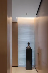 A modern hallway featuring a metallic bust sculpture mounted on a marble pedestal, with a vertical light strip behind it.