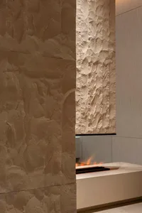 A modern minimalist fireplace with concrete walls and a fire burning inside.