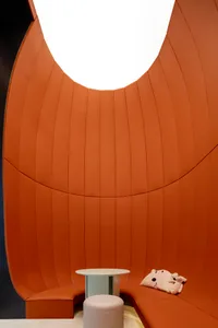 一间现代极简主义等候区，橙色皮革沙发环绕圆形天花板开口，配有圆形白色小桌和浅灰色圆形脚凳。