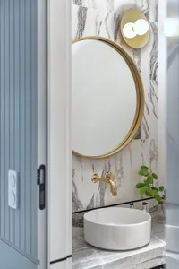 Modern bathroom with white marble tiles, circular sink, gold faucet, and round mirror.