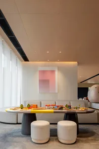A modern living room featuring comfortable cushions on a couch and two ottomans, with a large window and a colorful toy train