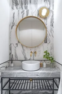 A modern bathroom with marble tiles features a circular mirror, a white sink, and brass accents.