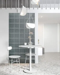 Modern minimalist dining space with white table, chairs, and decorative vase against a textured glass wall.
