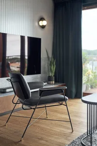 A modern minimalist living room featuring a wooden floor, black leather armchair, and a large window with green curtains.
