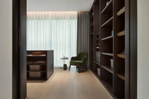 A modern walk-in closet with wooden shelves and a green upholstered chair.