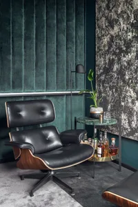 Modern living room featuring a black leather armchair with wooden accents and a side table with drinks and plants.