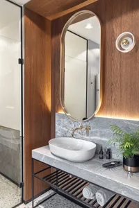 Modern minimalist bathroom featuring a white porcelain sink basin, brass faucet, oval-shaped brass-framed mirror above, terra