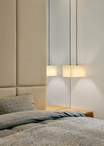A minimalist bedroom featuring a bed with a wooden headboard and a textile comforter, illuminated by pendant lights with beig