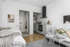A minimalist apartment featuring white marble countertops, walnut furniture, and a modern kitchen with a small kitchenette.