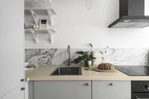 Minimalist kitchen featuring a marble backsplash and wooden countertop with a bread loaf and cutting board on the counter.