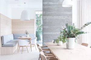 Modern dining room featuring a concrete-textured wall and a natural wood dining table adorned with greenery.