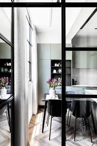 An industrial-style dining room with steel chairs, wooden flooring, and large windows for natural light.