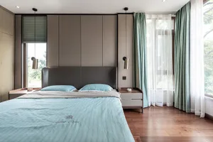 A contemporary minimalist bedroom with a grey leather headboard, blue bedding, and green curtains.