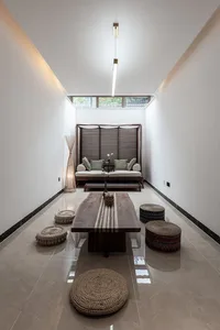 A minimalist living room featuring a wooden table, fabric poufs, and tiled flooring.