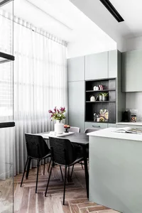 A modern dining kitchen with light wood flooring, a black table, black chairs, and light green cabinets.