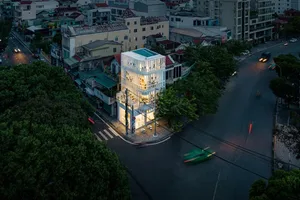 A modern glass building exterior at dusk with illuminated windows and a green car on the street.