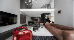 A modern industrial living room featuring a black spiral staircase, red chairs, brown sofa, and glass coffee table.