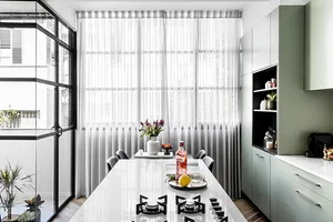 A contemporary kitchen with marble countertops, green cabinets, glass windows, and canvas wall art.