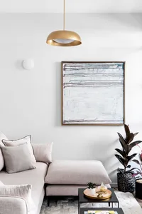 A modern living room with a beige sofa, pendant light, abstract art, and a small coffee table with a plant and candle.