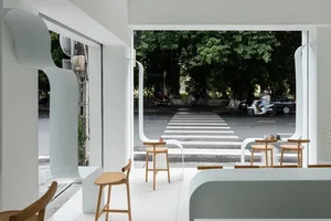 A minimalist coffee shop with modern white furniture and large windows showcasing the street view of the sidewalk.