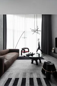 A modern minimalist living room with a brown leather sofa, a glass coffee table, and a black pendant light hanging above.