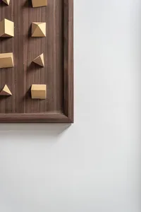 Gold-colored geometric shapes mounted on a wooden frame hanging on a white wall.