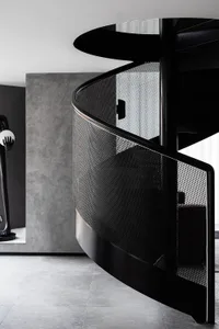 Industrial-inspired spiral staircase with a perforated metal balustrade and black metal handrail, set against a minimalist ba