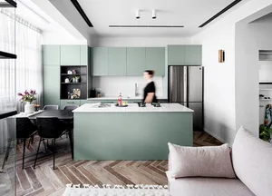 Modern minimalist kitchen with green cabinets, a central island with a marble countertop, and a white sofa in the foreground.