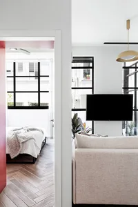 A minimalist living room with a neutral-toned sofa, a mounted TV, and herringbone-patterned flooring.