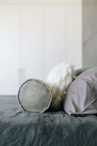 A minimalist bedroom with grey pillows and a plush white furry blanket on a bed with dark grey bedding.