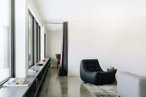 A minimalist living room featuring a black accent chair, grey sofa, and a mix of textures and materials, including concrete.
