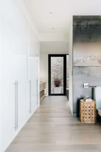 A modern, minimalist hallway with white cabinets, concrete flooring, and a black-framed entrance.