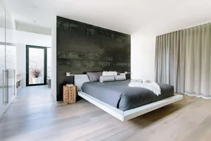 A modern minimalist bedroom featuring wooden flooring, a floating bed, and a dark accent wall.