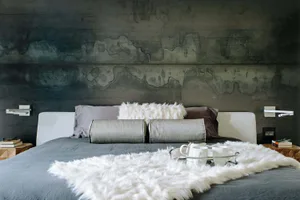 A minimalist bedroom with a faux concrete headboard and a plush white wool blanket, featuring modern and sleek design element