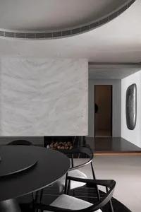 A modern, minimalist dining room featuring a fireplace with marble and black stone elements.